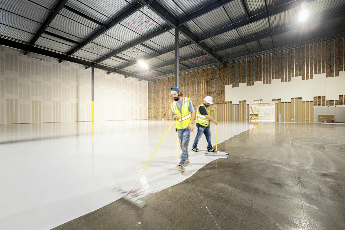 Two men sealing epoxy over warehouse concrete floor