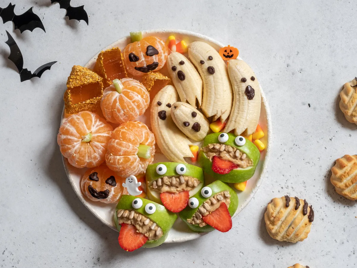 Halloween fruit platter with banana ghosts, mandarin pumpkins, and green apple monster mouths with strawberry tongues.