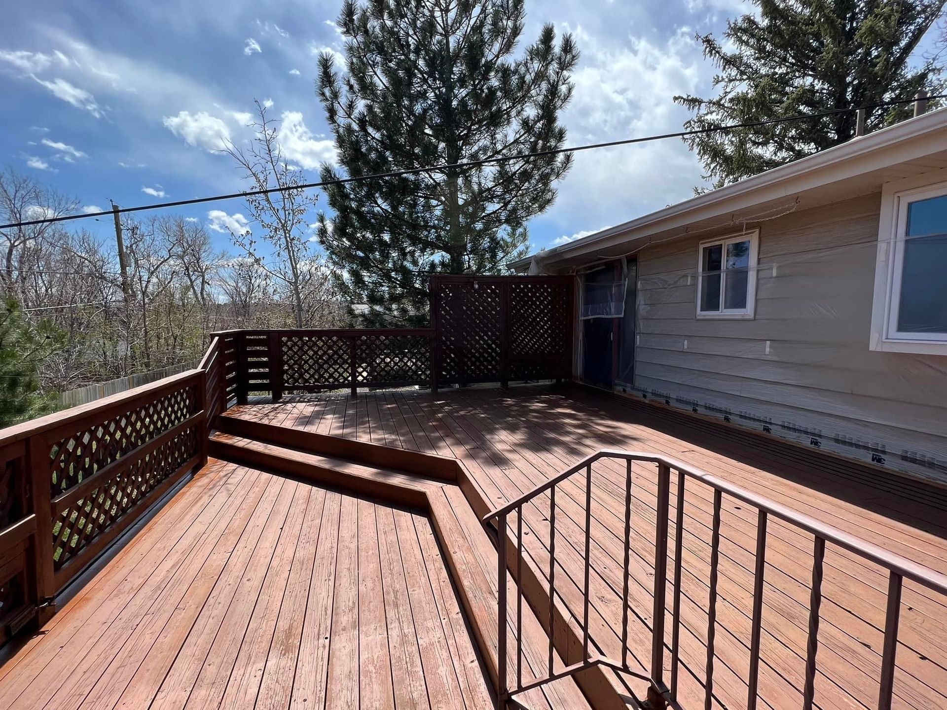 View of a house exterior with a multi-level stained wooden deck and fence.