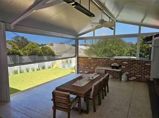 Modern outdoor living space featuring retractable blinds, creating shade and privacy for a backyard patio with dining table and chairs.