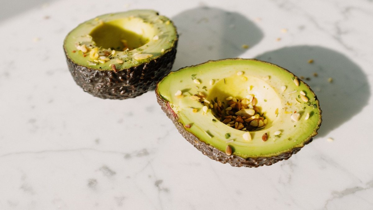 Halved ready-to-eat Hass avocado with its seed beside whole dark-skinned fruit, ripened evenly on an ethylene programme schedule