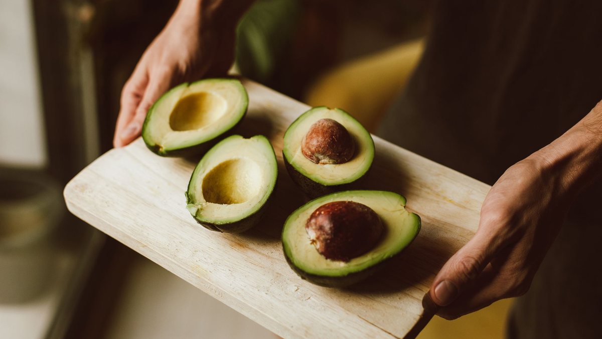 Chef slicing ripe Hass avocado halves on a wooden board in a commercial kitchen, the ready-to-eat fruit European buyers sell every week