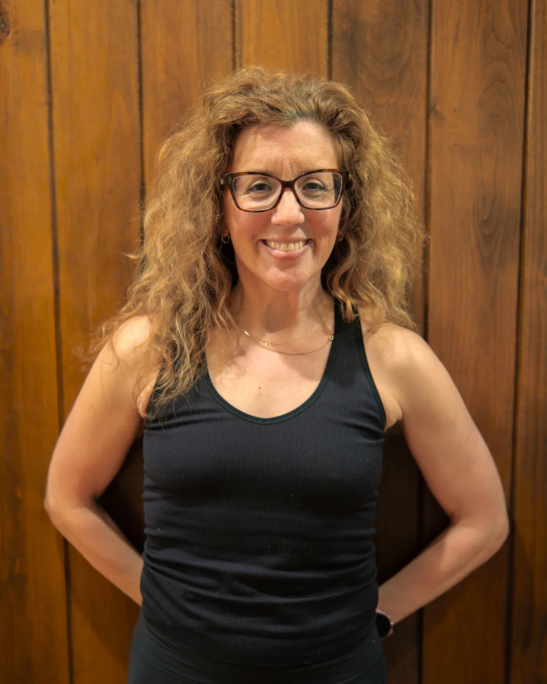 Confident female yoga teacher at Plymouth Yoga Room wearing glasses and a dark athletic tank top, smiling and ready to lead empowering yoga classes focused on strength, mindfulness, and holistic well-being.