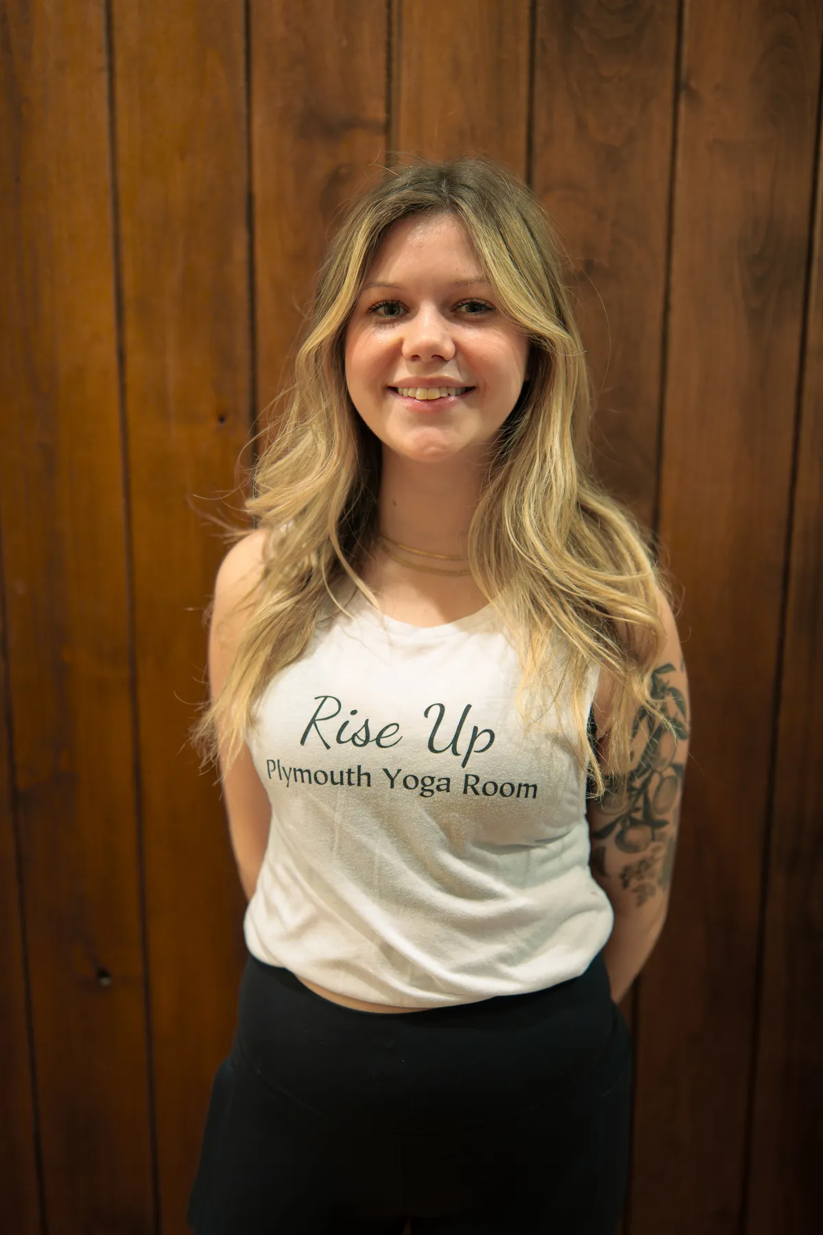 Smiling female yoga teacher at Plymouth Yoga Room wearing a black tank top, embodying positive energy and a commitment to guiding students through mindful yoga practices and holistic wellness.