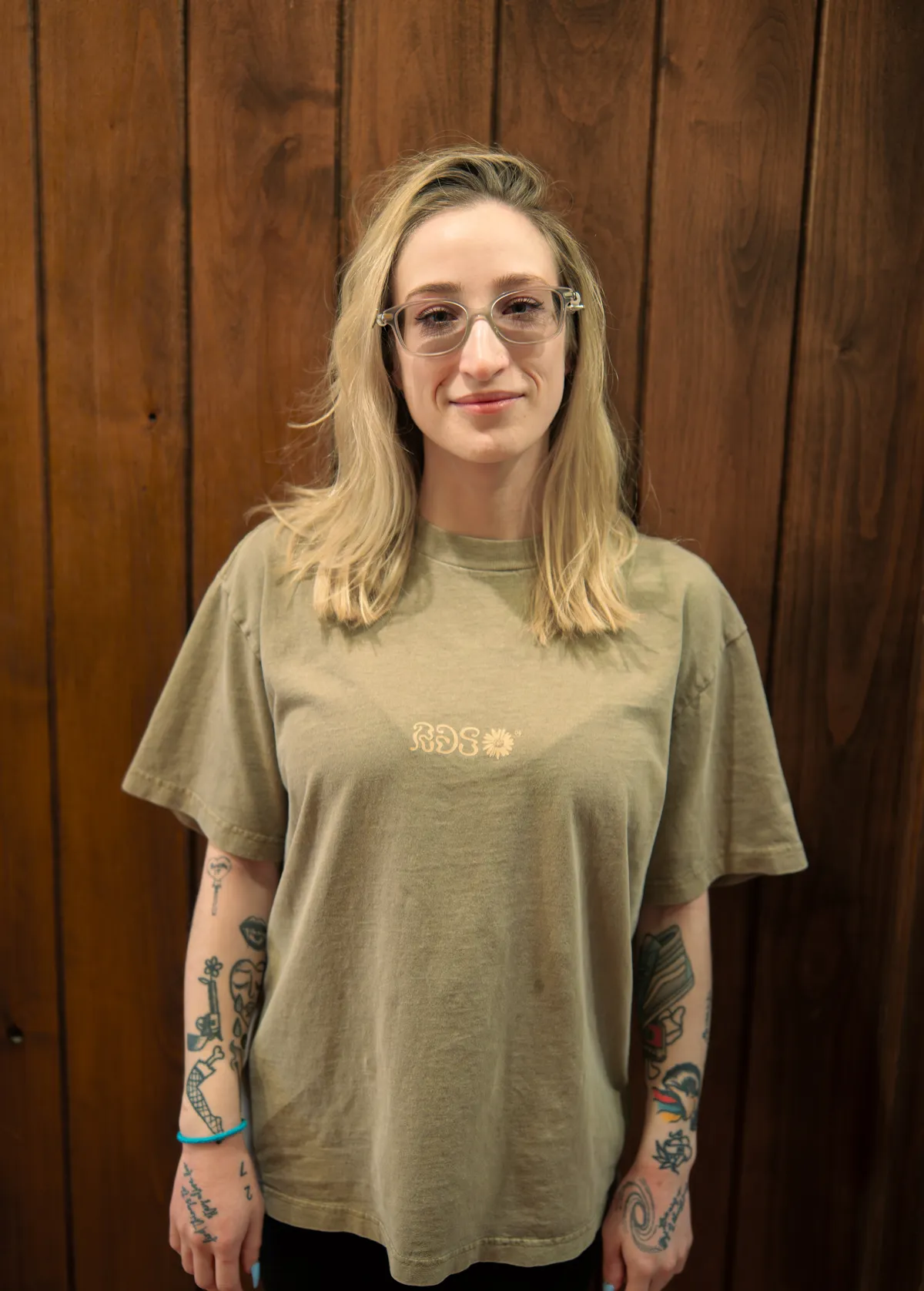Smiling female yoga teacher at Plymouth Yoga Room wearing a black crop top, standing confidently in front of a wooden wall, representing strength, grace, and a commitment to mindful movement and holistic wellness.