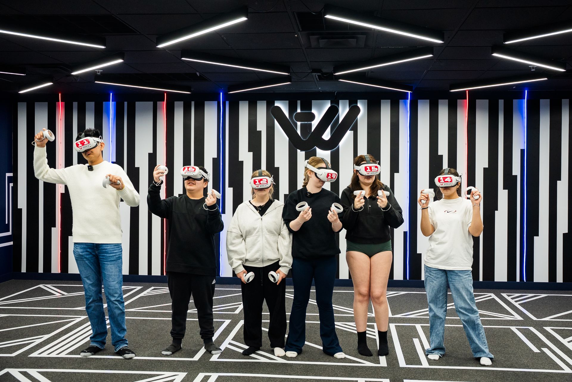 Six students in numbered headsets in front of the Another World logo wall