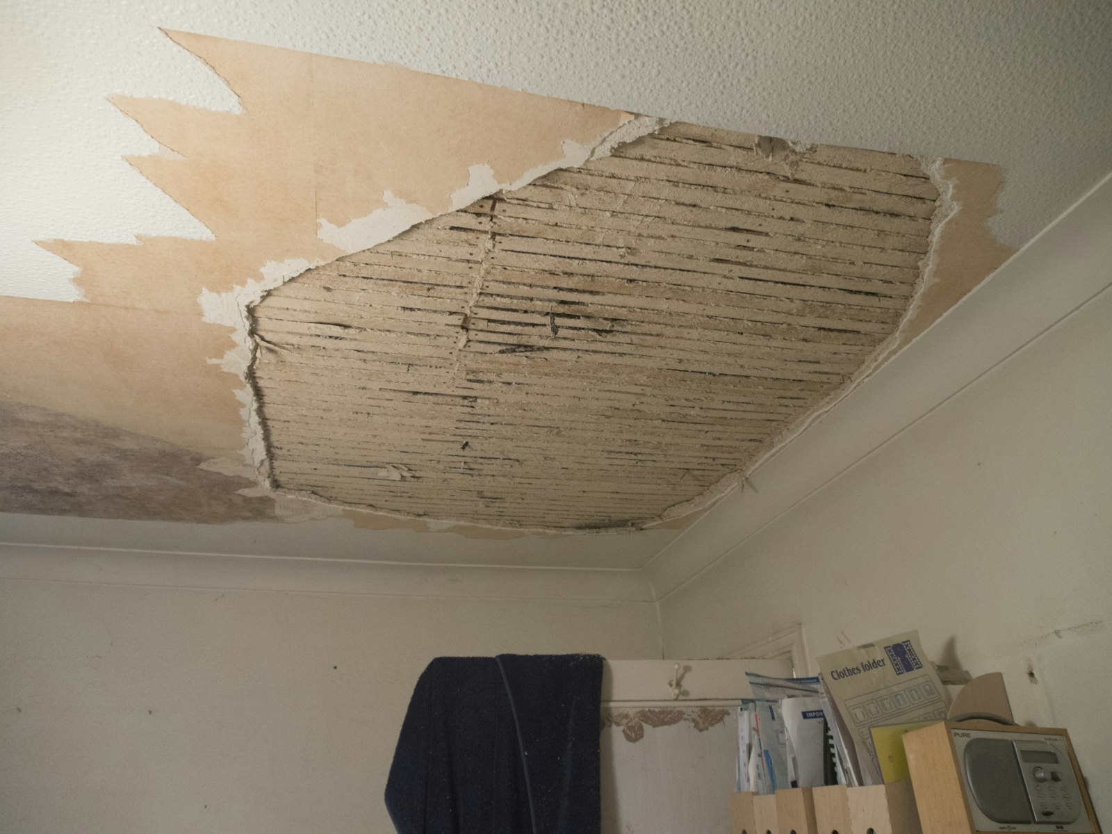 Water-damaged ceiling with drywall torn away exposing wood lath, showing interior damage from a facade or window leak in a residential unit
