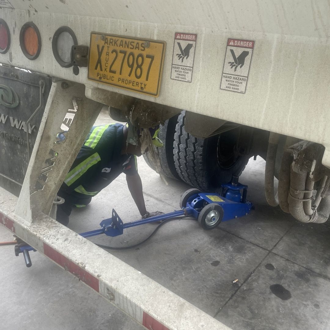Technician jacking up a trailer axle for truck tire service