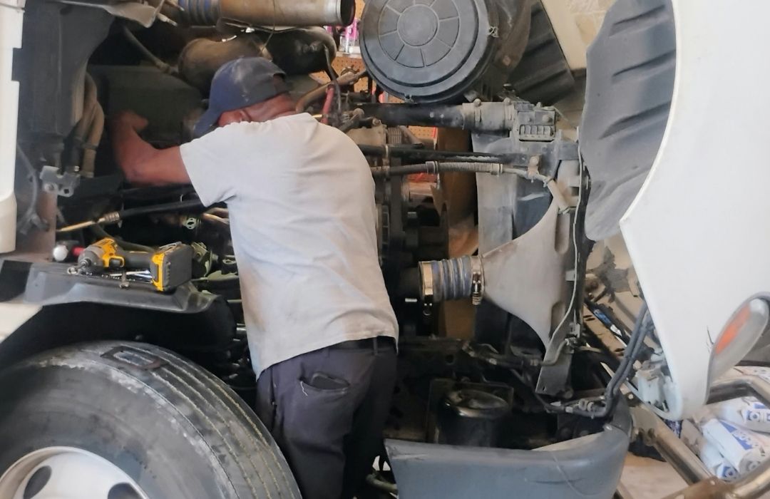 Mechanic repairing a diesel truck engine under the raised hood
