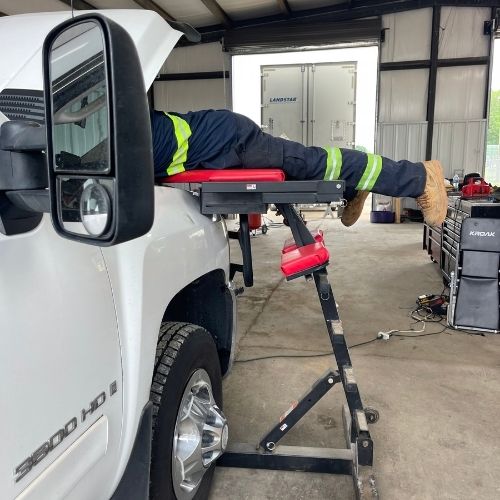 Mechanic using a fender creeper to work on a pickup truck engine
