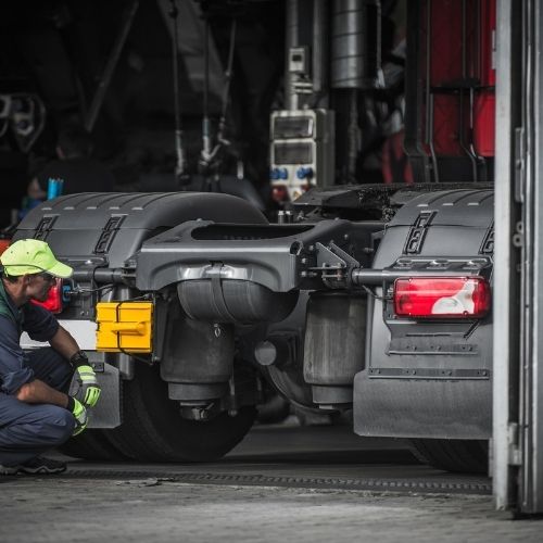 Technician inspecting the rear frame and lights of a truck in the shop