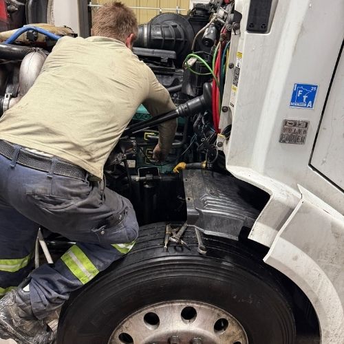 Mechanic repairing the engine of a white semi truck with the hood open