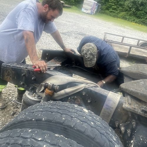 Two mechanics working on a truck chassis during a roadside repair