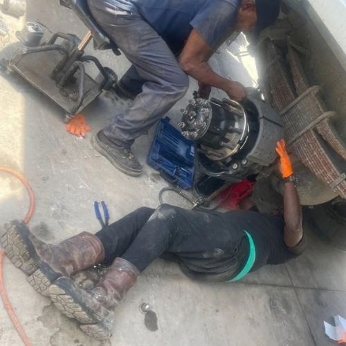 Mechanics servicing a wheel hub and brake assembly on the shop floor