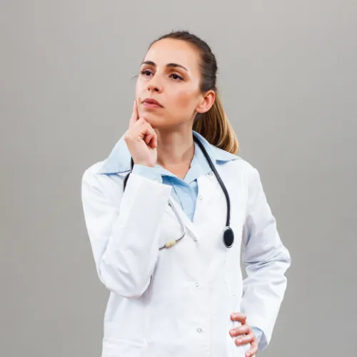Female doctor wearing a white lab coat and stethoscope, standing against a neutral grey background with a thoughtful expression. She is looking upward with one hand resting on her chin, suggesting contemplation or decision-making.