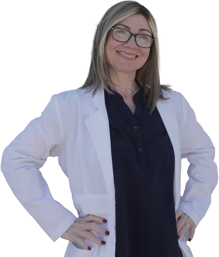 Smiling woman wearing glasses and a white lab coat over a dark blouse, standing confidently with hands on hips. She has straight, shoulder-length hair with highlights and is looking directly at the camera.