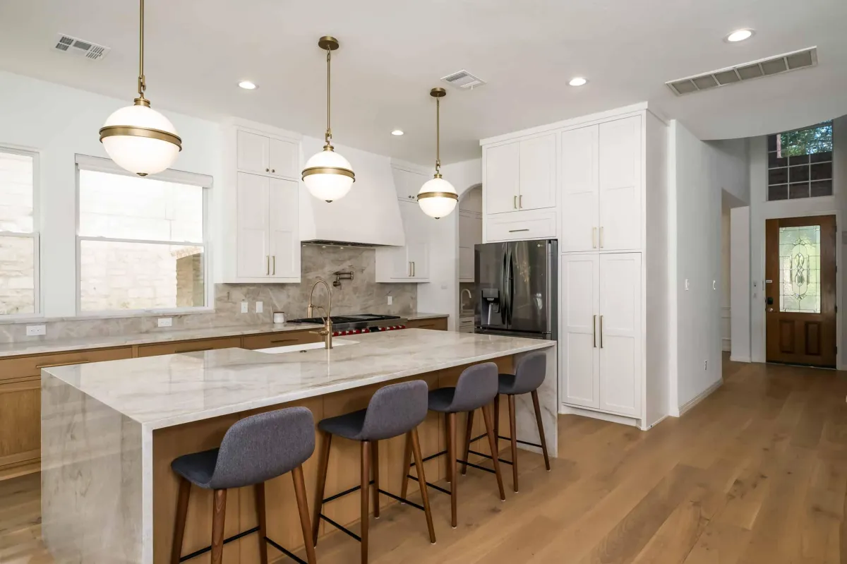 Remodeled kitchen with white cabinets, pendant lighting, large island, and wood flooring.