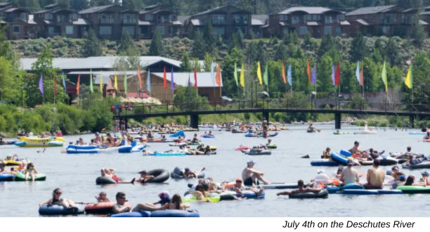 Dozens of people floating down a wide river on inner tubes, paddleboards, and inflatable rafts on a sunny summer day in Bend, Oregon.