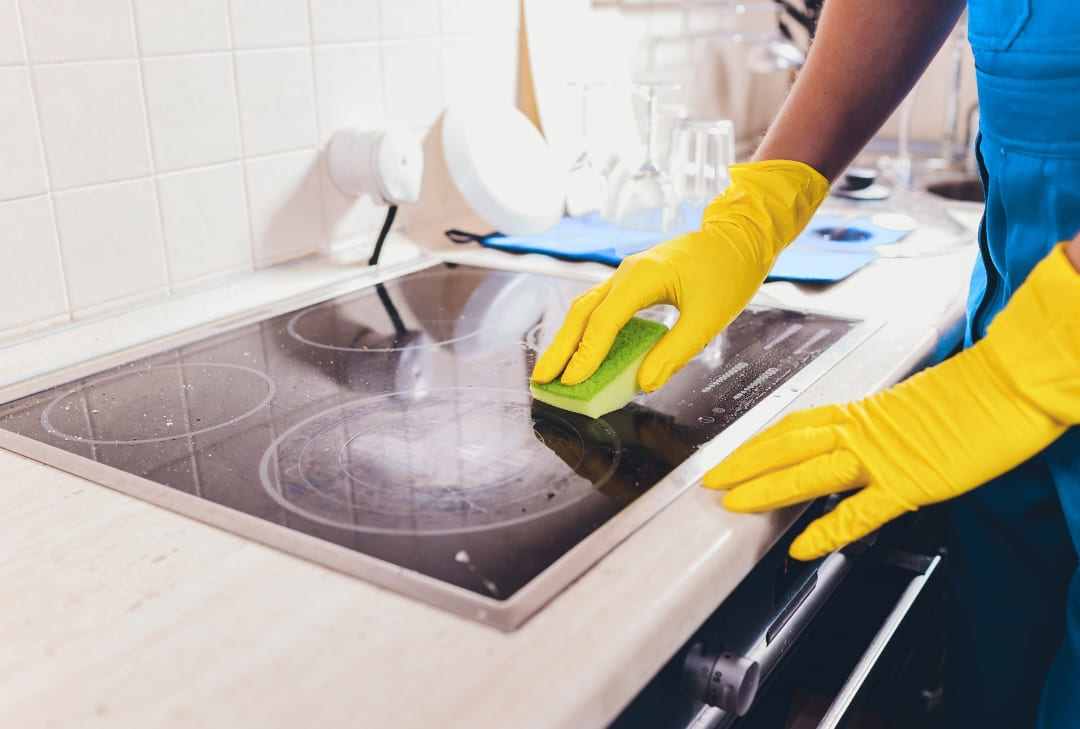 cleaner cleaning stove top with yellow gloves and a sponge