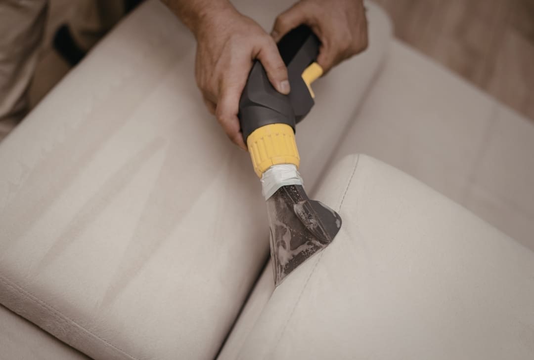 hands using an upholstery cleaning vacuum on a beige couch