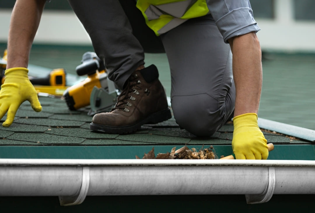 man on roof wearing yellow gloves cleaning out the house gutters