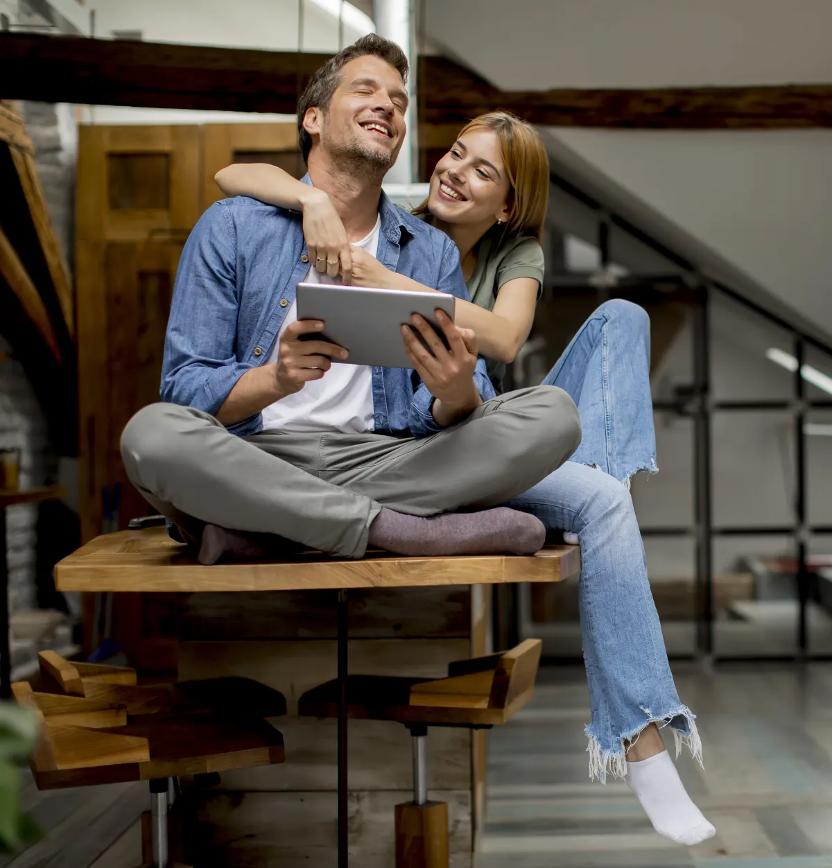 Happy first-time homebuyers relaxing at home and reviewing mortgage options on a tablet.
