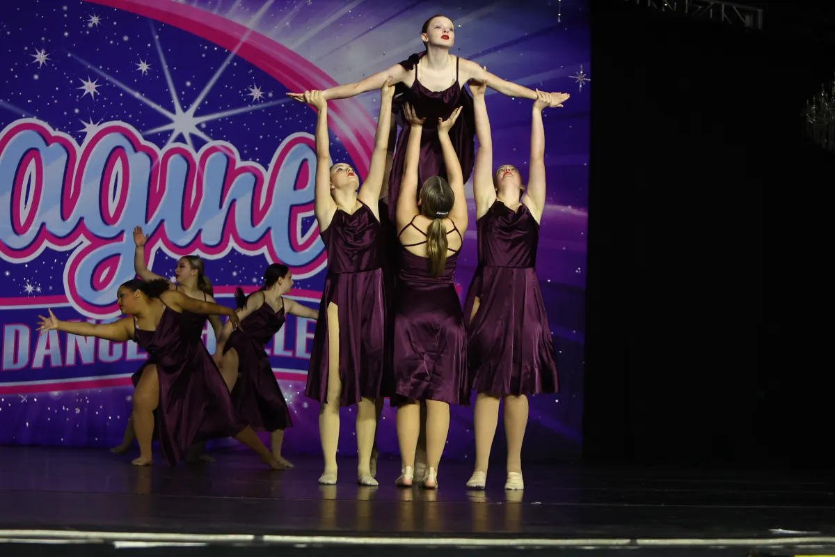 Dancers in burgundy costume on stage lifting a dancer