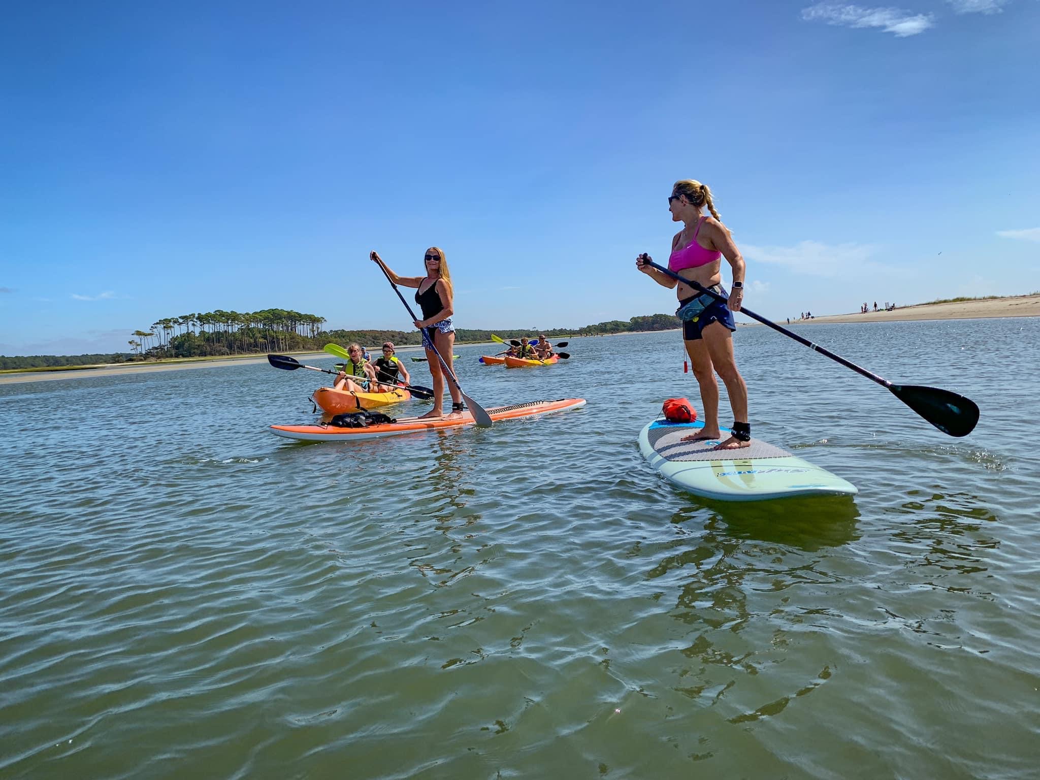 a group of women on paddleboards and kayaks on the water