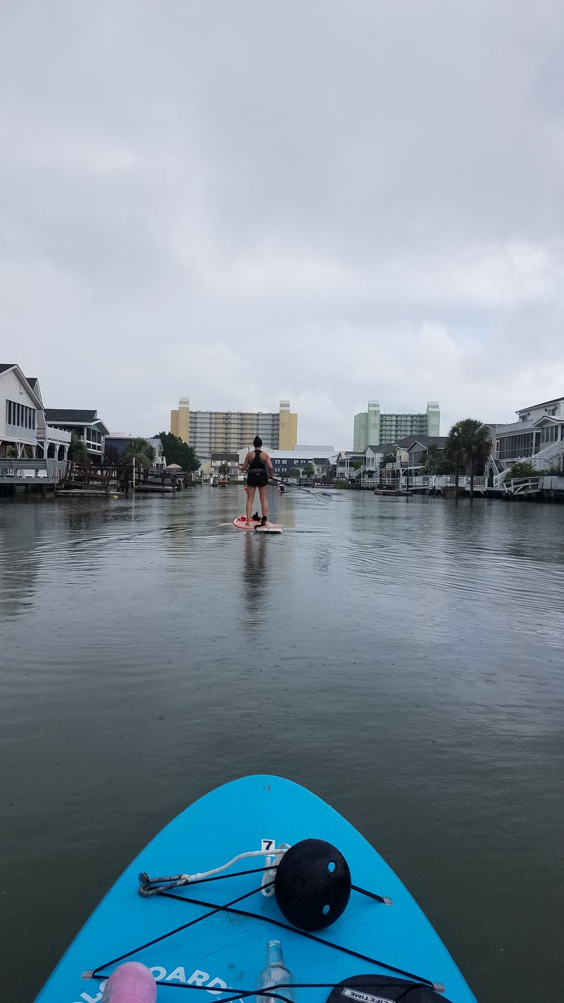 woman on a paddleboard paddling into the inlet facing condos and buildings in the background