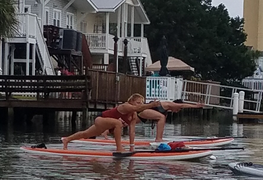 people on paddleboard doing yoga on the water with houses in the background