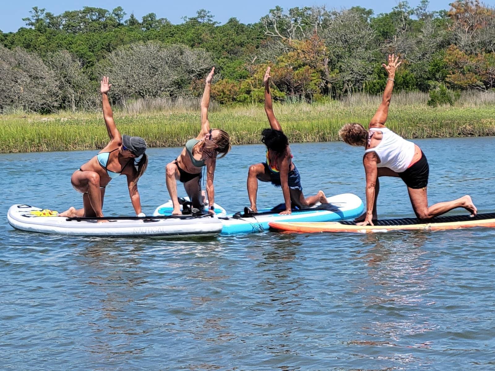 four women on paddleboard doing yoga on the water