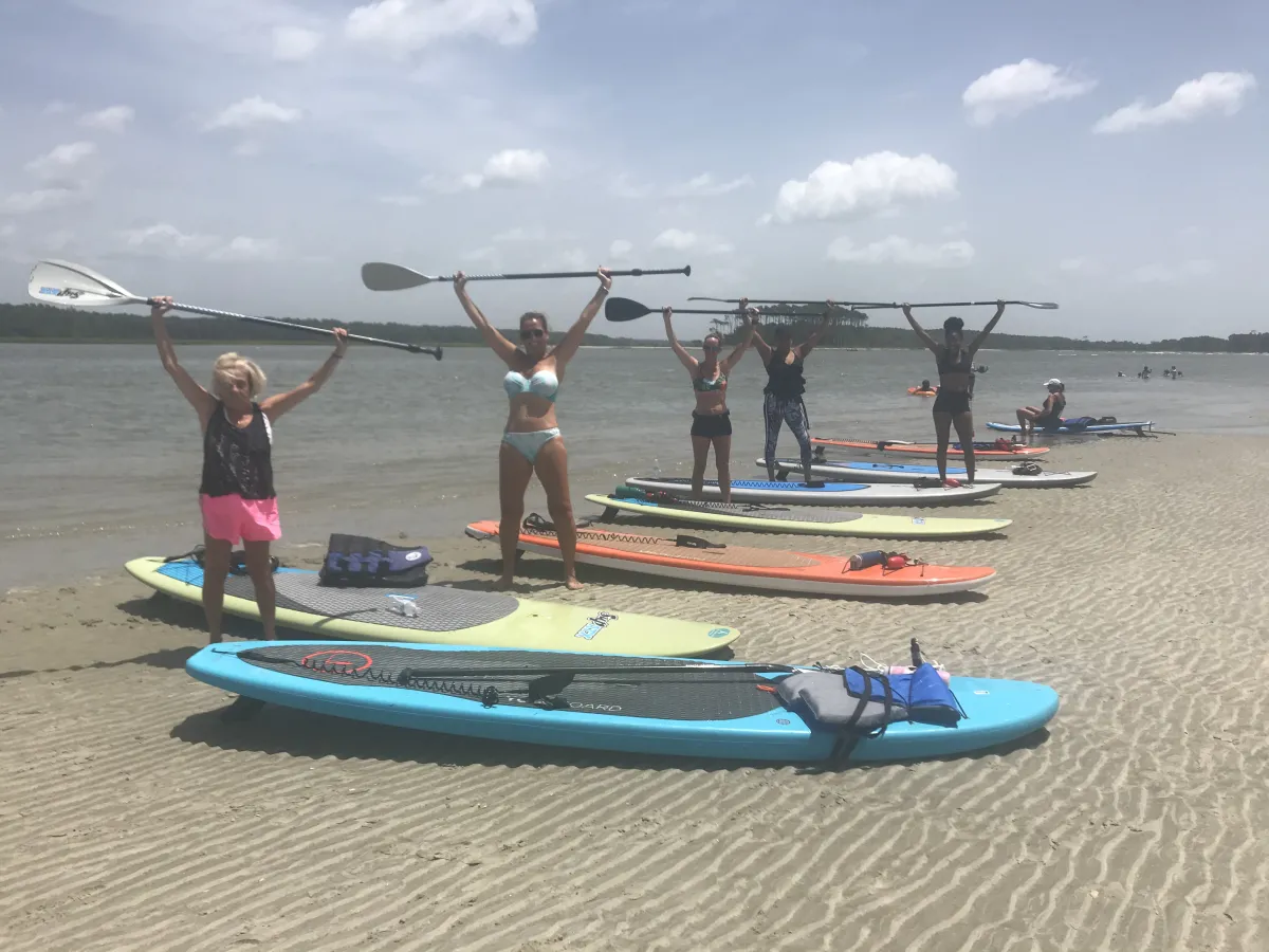 people on the beach with paddleboards holding oars in the air in celebration