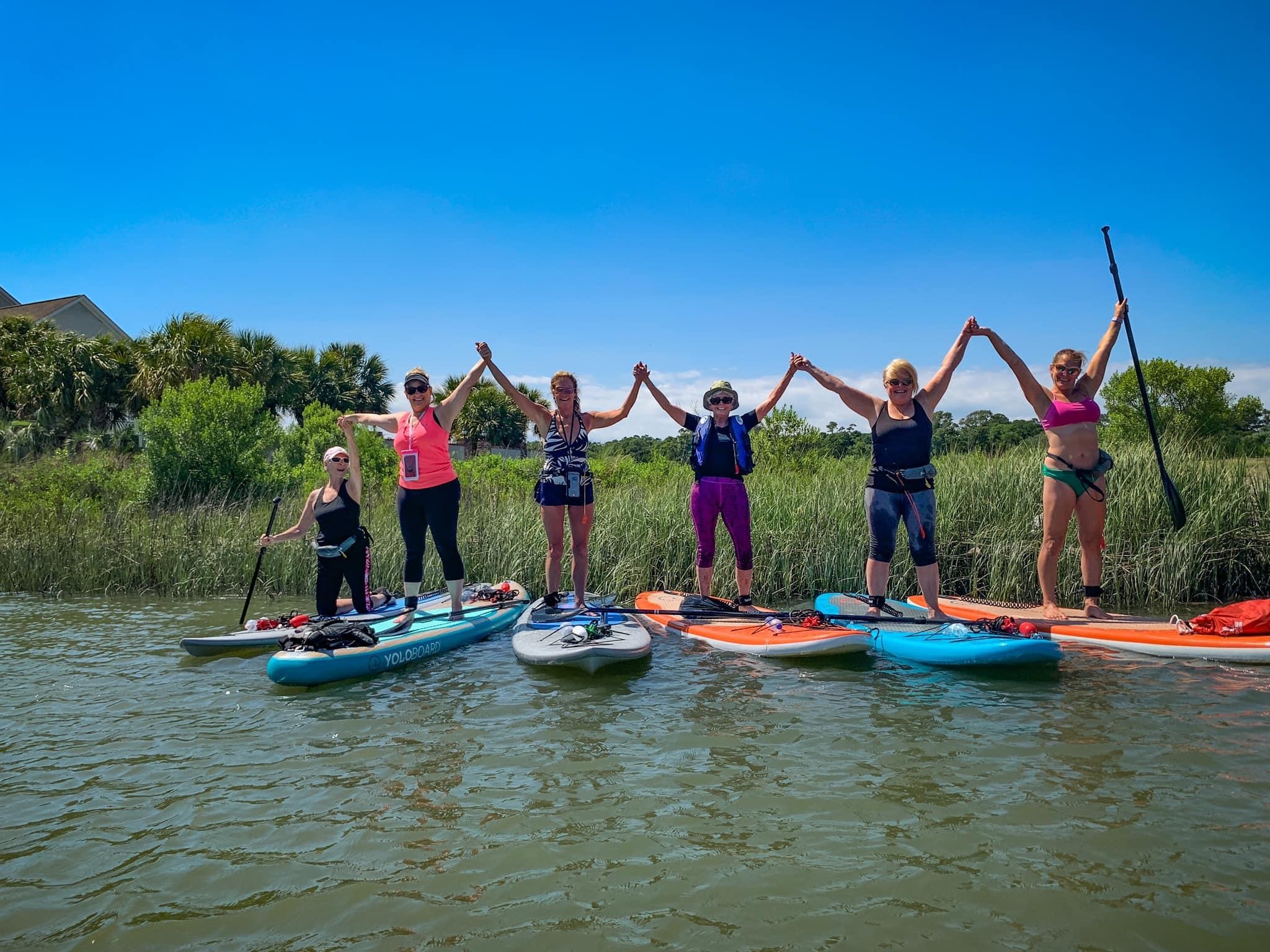 group of people on paddleboards raising their hands in joy on the water