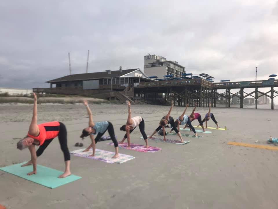 people doing yoga on the beach with a pier in the background