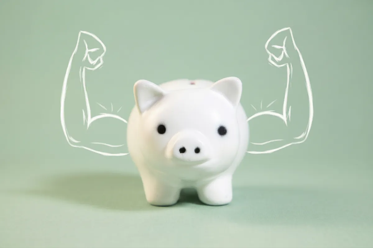 A white piggy bank with drawn muscular arms.
