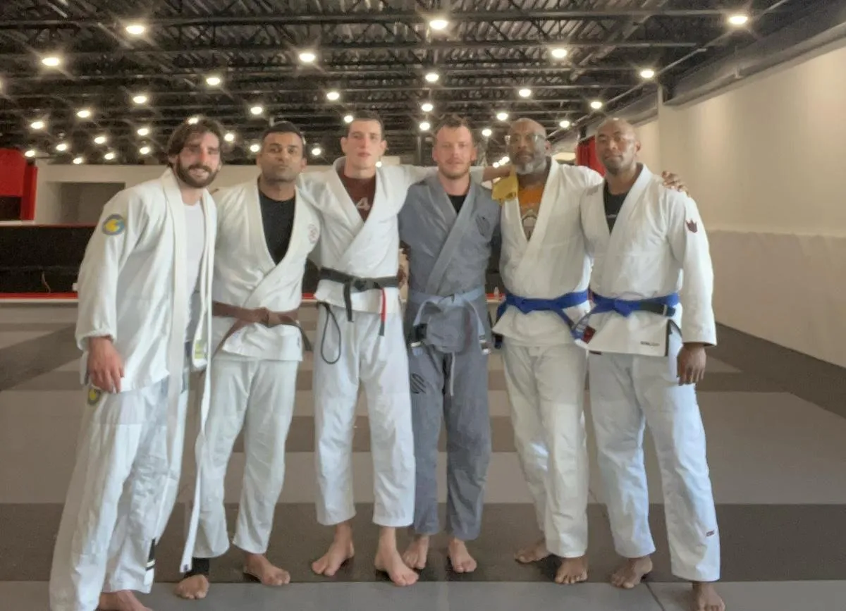 Group of martial arts instructors in gis, showcasing diverse belt ranks, in a well-lit Jiu-Jitsu training facility, promoting community and skill development at New Wave Jiu-Jitsu in Indianapolis.