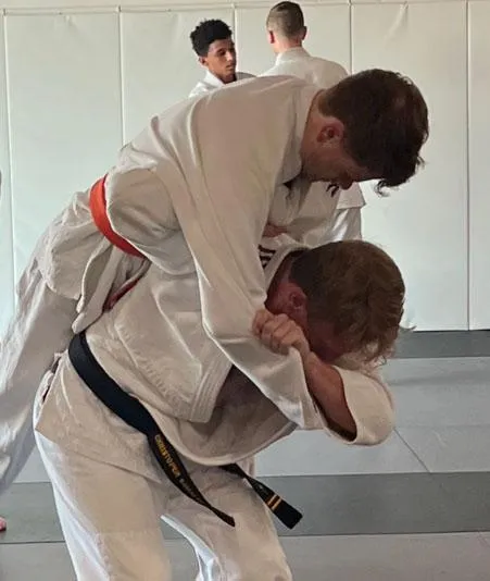 Two practitioners engaging in Judo techniques on the mat, one executing a throw while the other defends, showcasing skill and physical fitness in a training environment.