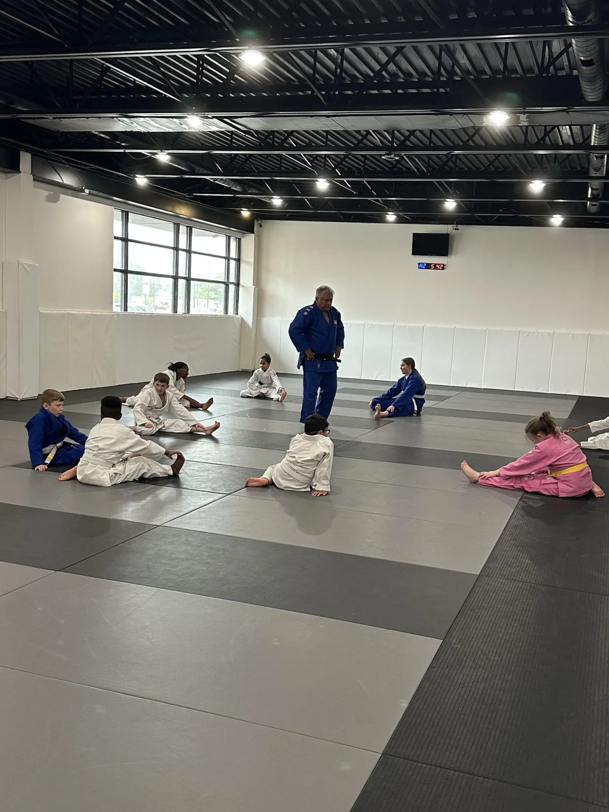 Children practicing Judo in a training facility, guided by an instructor in a blue gi, focusing on skill development and discipline.