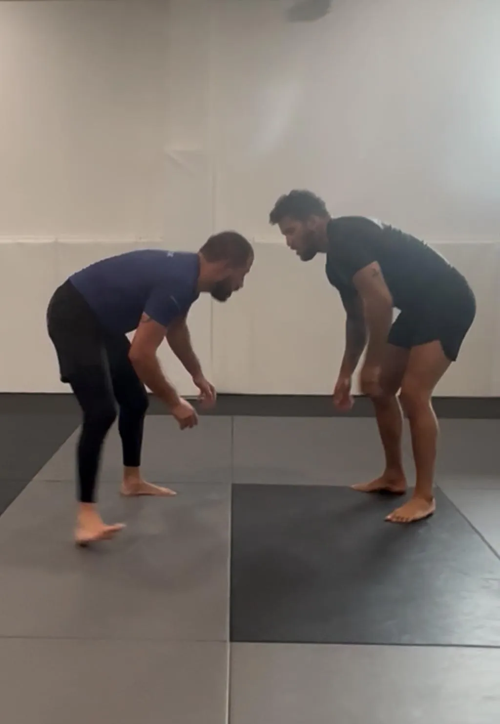 Two grapplers in a wrestling stance on a mat, focused on takedown techniques in a beginner wrestling class for ages 13 and up at New Wave Jiu Jitsu.