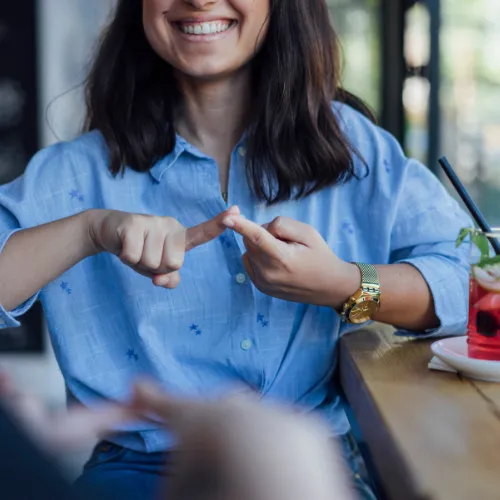 A smiling woman in a blue shirt showing her hand with fingers pointed while seated at a table, indicating excitement about the upcoming Pre-ETS and Early Steps program.