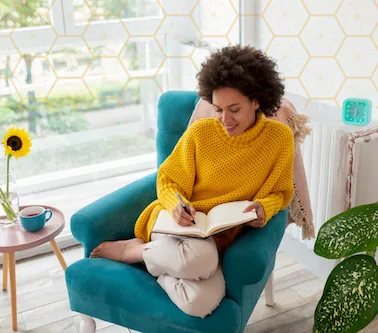 lady sat in teal coloured chair wearing mustard jumper writing in a journal