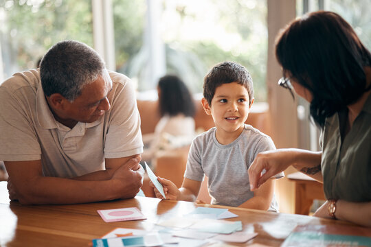 A young boy smiles at two supportive adults leaning in during a learning activity at a bright, welcoming table.