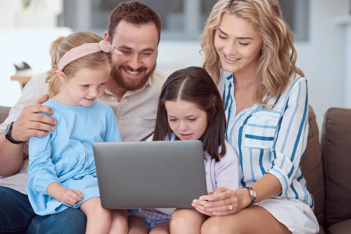 A family of four sitting, engaged in viewing a laptop screen.