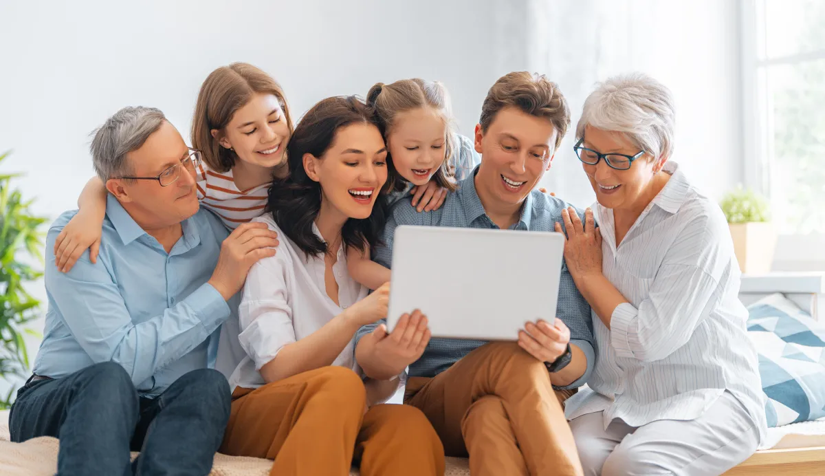 A family of four sitting together on a couch, engaged in viewing a laptop screen.