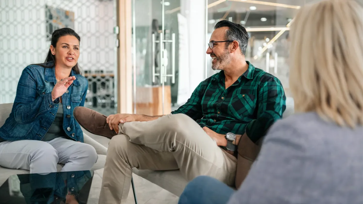 A casual, collaborative executive coaching discussion among three leaders in a modern office lounge setting.