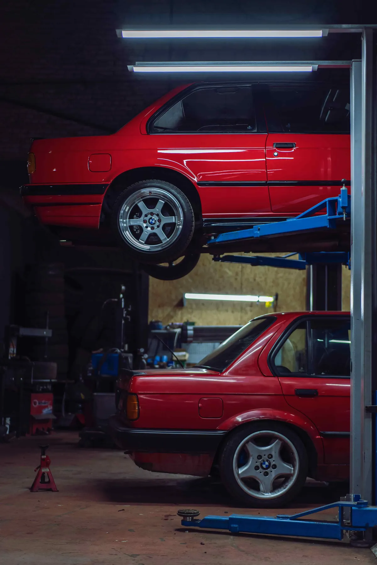 two bmw's are parked inside a auto mechanic shop garage, one is on a lift