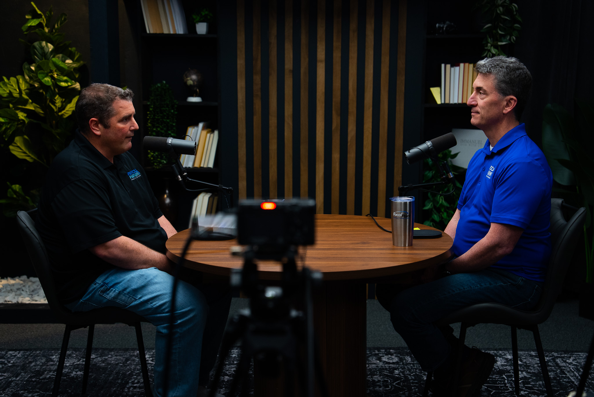 Two podcasters in conversation at a studio table during a recording session