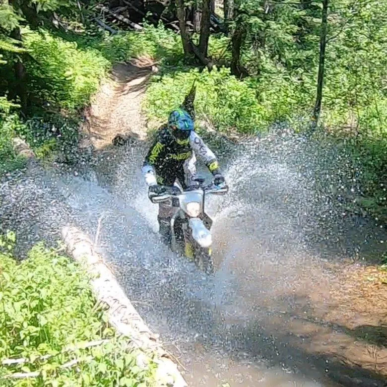 Person riding a dirt bike through a forest water crossing on a cleared off-road trail in Oklahoma.