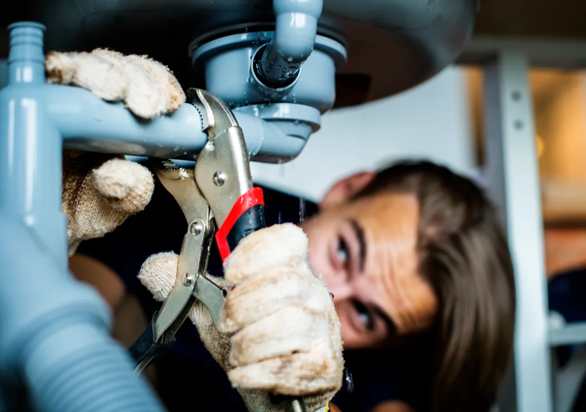Plumber adjusting pipe under sink with wrench, diagnosing misaligned joints causing sewer backups.