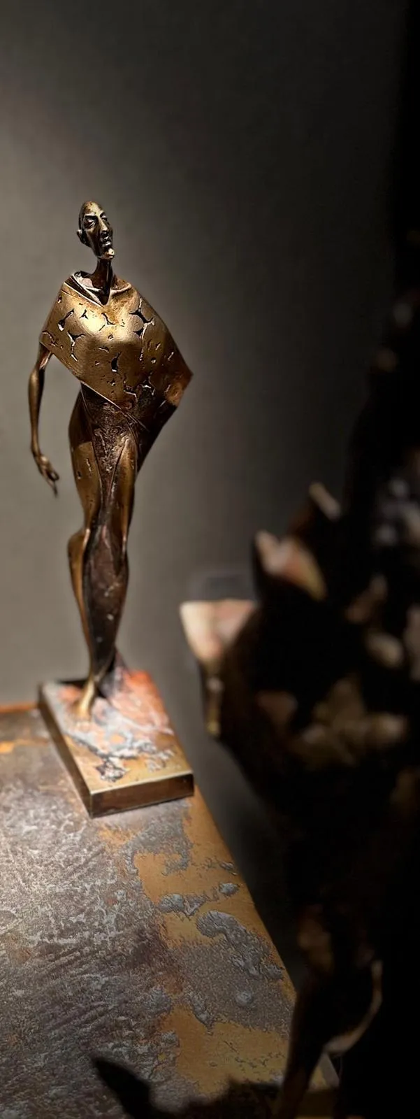 Skulptur „Herbst“ aus CuSi3 Siliziumbronze (ca. 25 cm) auf Metallplatte; schlanke, abstrahierte Figur im Vordergrund mit nach oben gerichtetem Blick, dahinter zwei weitere Figuren unscharf vor grauer Galeriewand.